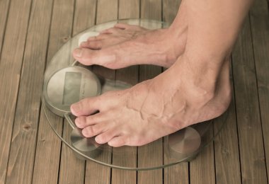 Adam ölçekler üzerinde duruyor. Erkek ayakları cam ölçekler ve ahşap zemin üzerinde