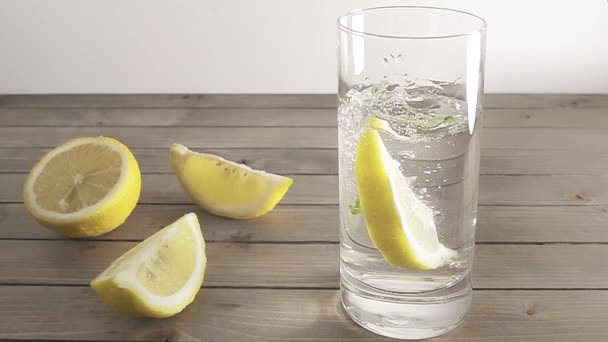 Pezzo di limone che cade in vetro trasparente di acqua minerale con menta. L'acqua schizza nel bicchiere. Rallentatore . — Video Stock