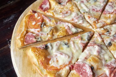 Siyah ahşap arka planda kesilmiş sosisli ve domatesli pizza.