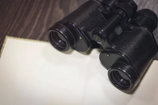 vintage binoculars on a dark wooden background with an open book with blank blank pages