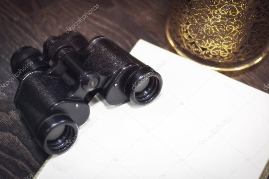 vintage binoculars on a dark wooden background with an open book with blank blank pages