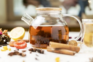 Baharat ve kuru meyvelerden oluşan beyaz bir masada siyah çay ile cam çaydanlık.