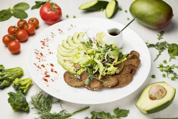 fresh vegetable salad light salad on a large white plate on a white table with a composition of tomatoes, avocado, parsley, cucumber, peas, broccoli