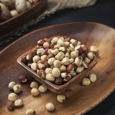 Kare bir ahşap kasede fındık ve arka planda oval ahşap tepsi ve çuval bezi.