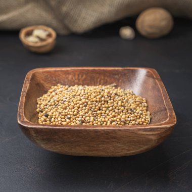 Kare bir ahşap kase üzerinde baharatlar ve taneler koyu bir arka planda ve çuval bezi