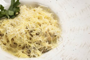 Tagliatelle makarnası, tavuklu ve mantarlı yuvarlak beyaz tabakta.