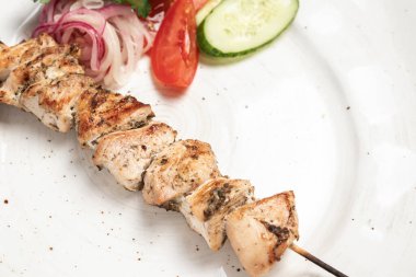 Sebzeli tavuk şişi domates ve beyaz tabakta salatalık dilimleri.