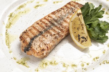 Beyaz tabakta bir dilim limonla ızgara somon.