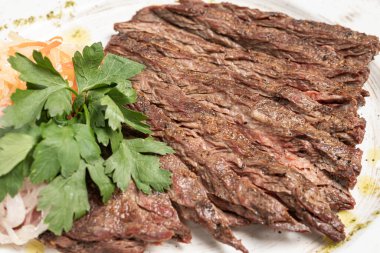 Biftek, beyaz bir tabakta sebzelerle dilimlenmiş.