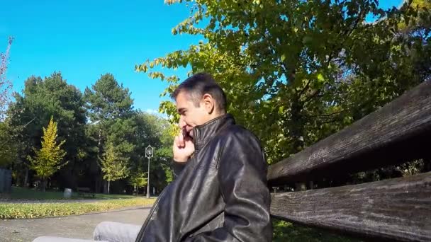 Az ember ül a padon őszi parkban használ sejt telefon — Stock videók