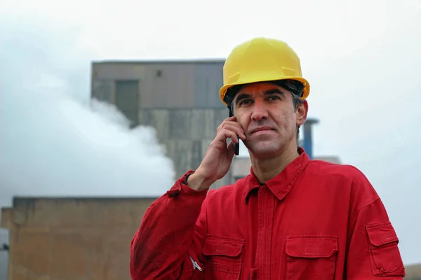 Werknemer met behulp van slimme telefoon met fabriek op de achtergrond — Stockfoto