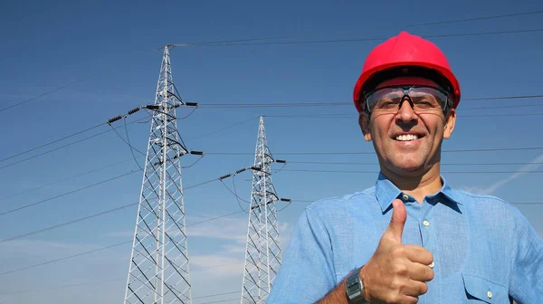 Trabajador sonriente cerca de las torres de transmisión eléctrica — Foto de Stock