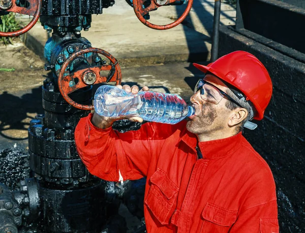 Нефтепромышленник пьет воду рядом с нефтяной скважиной — стоковое фото