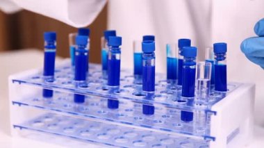 Test tüpleri rafa yerleştirerek laborant. Araştırmacı mavi koruyucu eldiven giymiş. Pipet, içine bir tüp ile reaktif mavi örnek bırakarak kullanarak el görünümünü kapat.