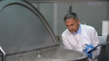 Süt bitkisi teknolojisi uzmanı süt pastörizasyon sürecini kontrol ediyor. Süt İşleme Tesisinde Süt Pastörizasyonu. Pastörizasyon tankının içindeki süt. Mandıra Gıda Güvenliği.