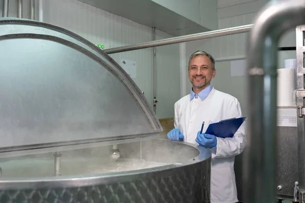 Χαμογελώντας Dairy Plant Food Engineer στέκεται δίπλα από ανοξείδωτο χάλυβα παστεριωτήρα γάλακτος δεξαμενή — Φωτογραφία Αρχείου