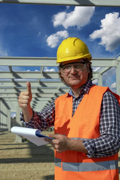 Trabajador de la construcción con portapapeles cediendo el pulgar en el sitio de construcción —  Fotos de Stock