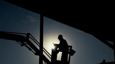 Yükseklerde çalışan bir kova hidrolik mobil inşaat platformunda bakım işçisi. Gün batımında inşaat işçisinin silueti. İşçi Hidrolik İnşaat Platformunu İşletiyor.