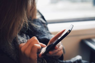 Trenin penceresinin yanında akıllı telefonunu kullanan genç bir kadın.