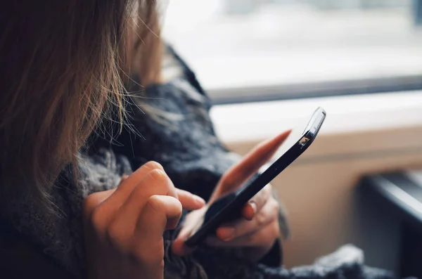 Trenin penceresinin yanında akıllı telefonunu kullanan genç bir kadın.