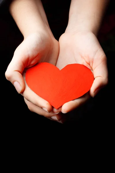 Rotes Herz in den Handflächen eines Kindes vor dunklem Hintergrund. — Stockfoto