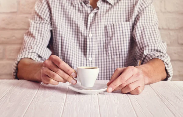 Pause café. Homme assis sur la table blanche avec une tasse d'espresso dans la chemise à carreaux. Fond mural en briques blanches — Photo