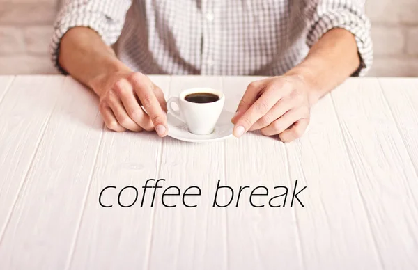 Pausa para café. Homem sentado na mesa branca com uma chávena de café expresso na camisa marcada. Tijolos brancos parede fundo — Fotografia de Stock