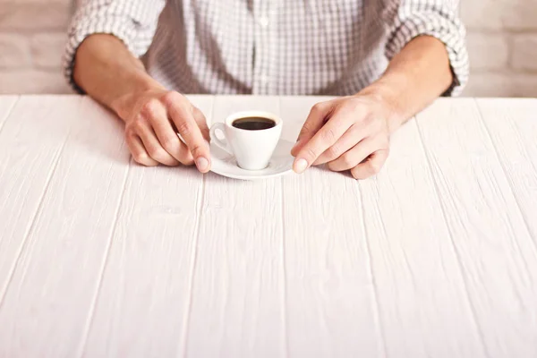 Pause café. Homme assis sur la table blanche avec une tasse d'espresso dans la chemise à carreaux. Fond mural en briques blanches — Photo
