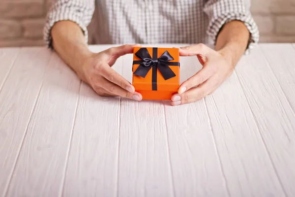 Begrip van de liefde. Man met oranje cadeau met een zwart lint in handen. Dag van de vrouw. St. Valenine de dag Rechtenvrije Stockafbeeldingen