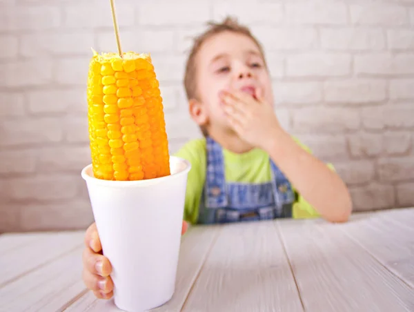 Leuke jongen holdind gekookt suikermaïs in cup op witte bakstenen muur achtergrond Stockfoto