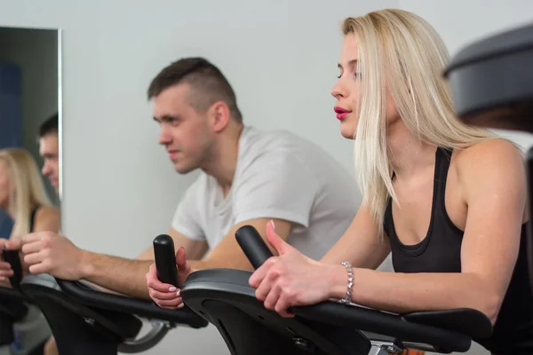 Jovem e mulher de bicicleta no ginásio, exercitando as pernas fazendo bicicletas de ciclismo de treino cardio — Fotografia de Stock
