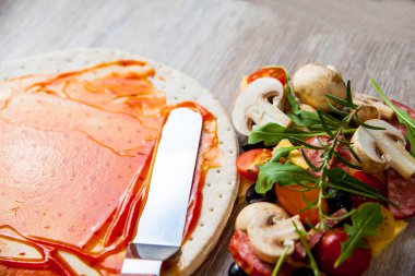 Ketçap ve pizza için malzemeler hamur olarak kaplı. Ahşap bir masaya