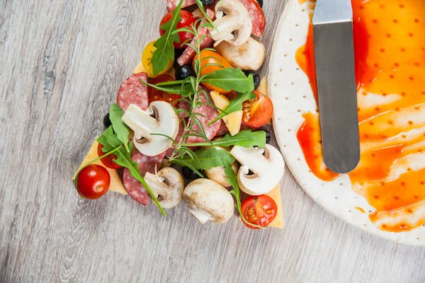 Base de pâte recouverte de ketchup et d'ingrédients pour pizza. Sur une table en bois — Photo