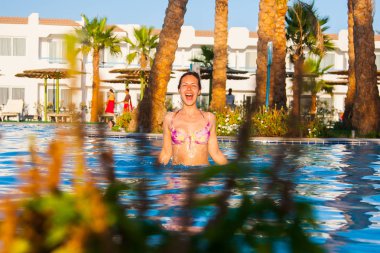 Yüzme Havuzu ve palmiye ağaçları arka plan ile plaj bikini mayoyla poz mutlu genç kadın