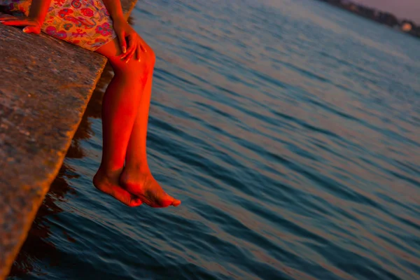 美丽的女人，看着夕阳坐在靠近水的地方 — 图库照片