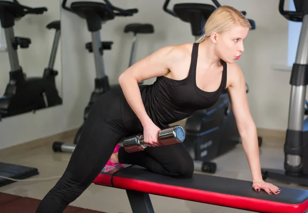 Sexy junge Leichtathletin bei Pressübungen mit Hanteln. Fitness muskulöse Frau in schwarzer Sportkleidung trainiert auf Bank im Fitnessstudio Stockbild