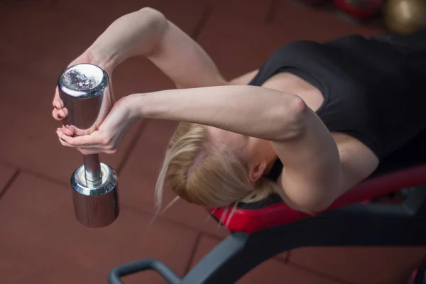 Sexy jovem atlética menina fazendo halteres imprensa exercícios. Fitness mulher musculada em preto esporte roupas treino no banco no ginásio — Fotografia de Stock