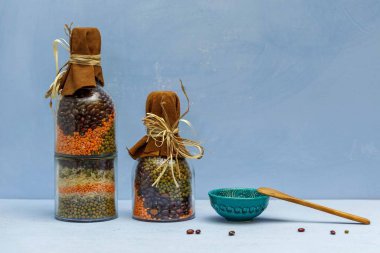 Farklı renkte fasulye ve mercimek içeren iki kavanoz mavi arka planda, yatay, uzay