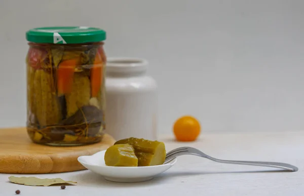 Sliced pickled cucumber on a white plate with a fork. Canned vegetables and a white can in the light background.