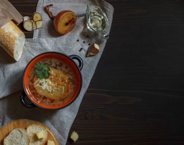 Olla con sopa de cebolla y croutons en una servilleta de lino con baguette sobre un fondo oscuro desde arriba con espacio — Foto de Stock