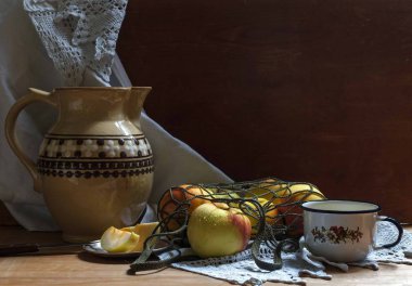 Bir sicim torbasında elmalarla ve arka planda beyaz havluyla boyanmış bir seramik sürahi ile hayat