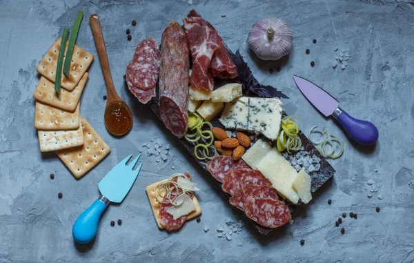 Salami, jamón ahumado, parmesano y roquefort sobre una tabla de mármol sobre un fondo gris, vista superior —  Fotos de Stock