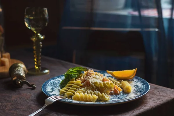 Painted plate with colorful pasta and parmesan on a brown tablecloth