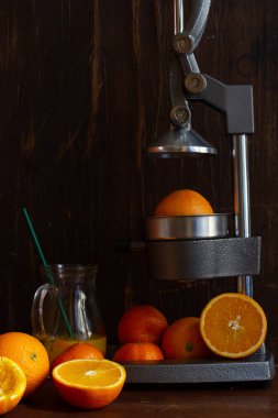 half an orange on a citrus press, sliced citrus and peel, jug of juice on a dark wooden background