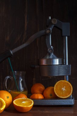 oranges and tangerines, sliced citrus and peel and citrus press on a dark wooden background