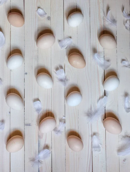 Light colored chicken eggs laid out on white boards in a pattern with white feathers