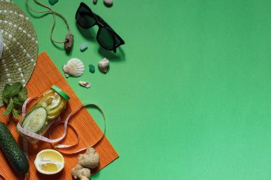 Flatlay with Sassi water, lemon and mint on orange bedding, centimeter in the tape, sunglasses, straw hat, shells and pebbles on a green background with space clipart