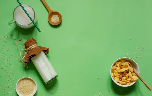 Vista superior sobre un fondo verde brillante con una botella de leche de arroz, copos de maíz y una jarra con espacio, horizontalmente — Foto de Stock