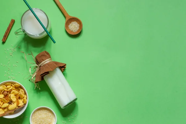 Top view on a bright green background with a bottle of rice milk, corn flakes and a jug with space,horizontally — Stock Photo, Image