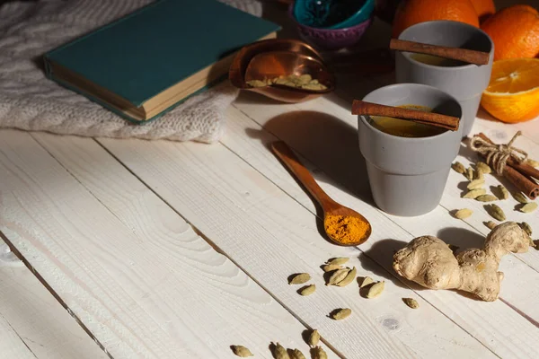 Tazas de té de jengibre en la mesa con naranjas, un libro y una manta de punto — Foto de Stock